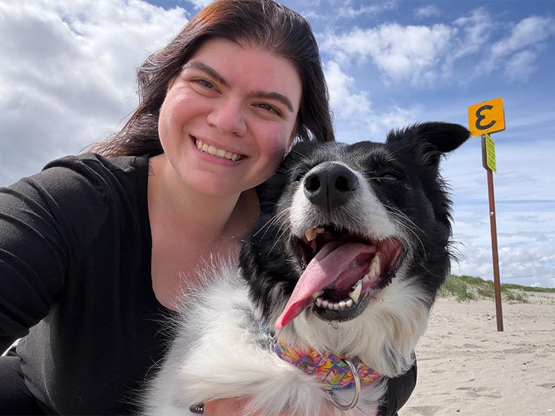 A woman with a black and white dog smiles at the camera